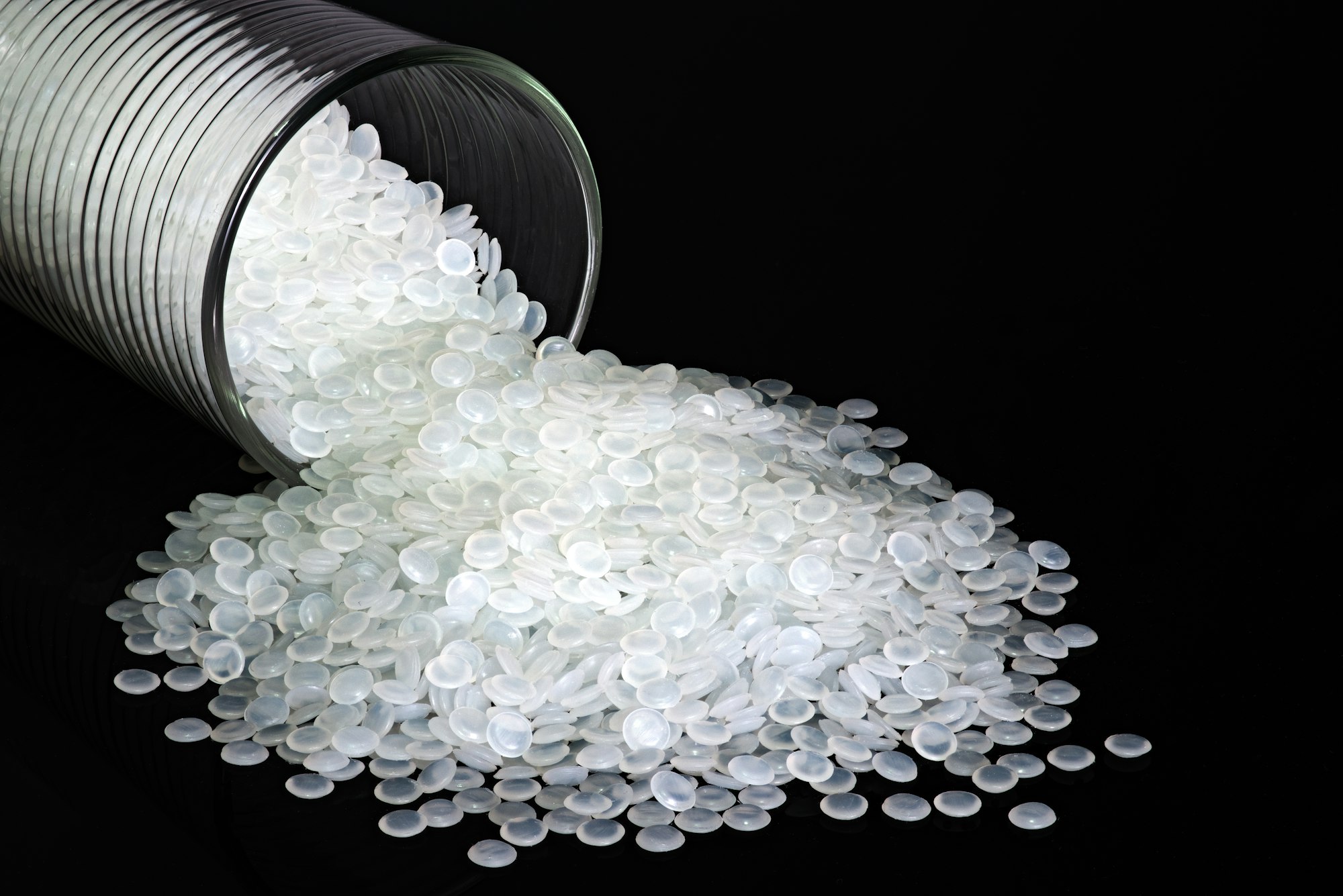 Industrial white plastic beads, granules on black background.